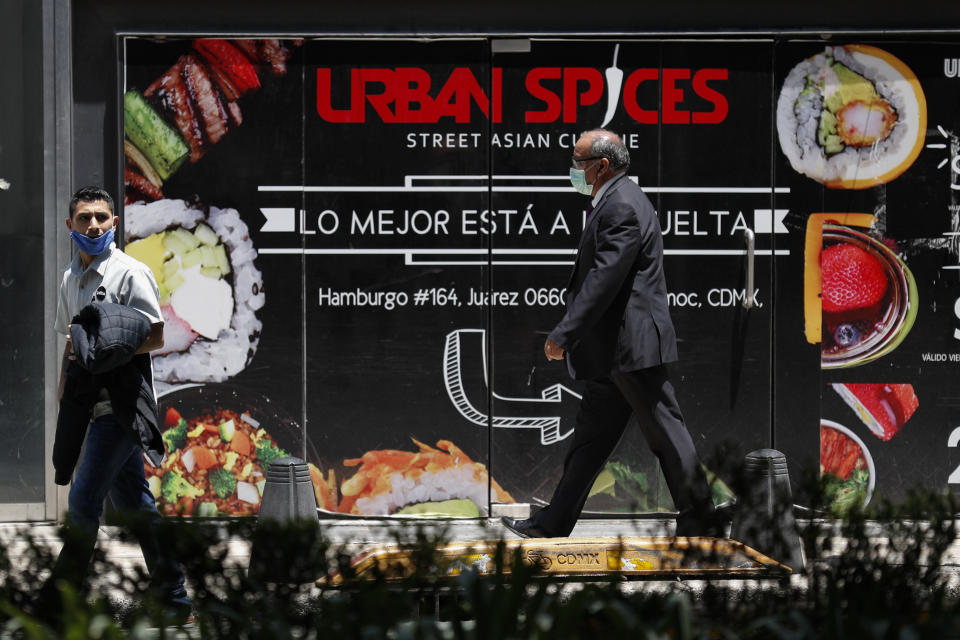 People wearing face masks walk past a sign advertising a restaurant in Mexico City, Friday, June 5, 2020. (AP Photo/Rebecca Blackwell)