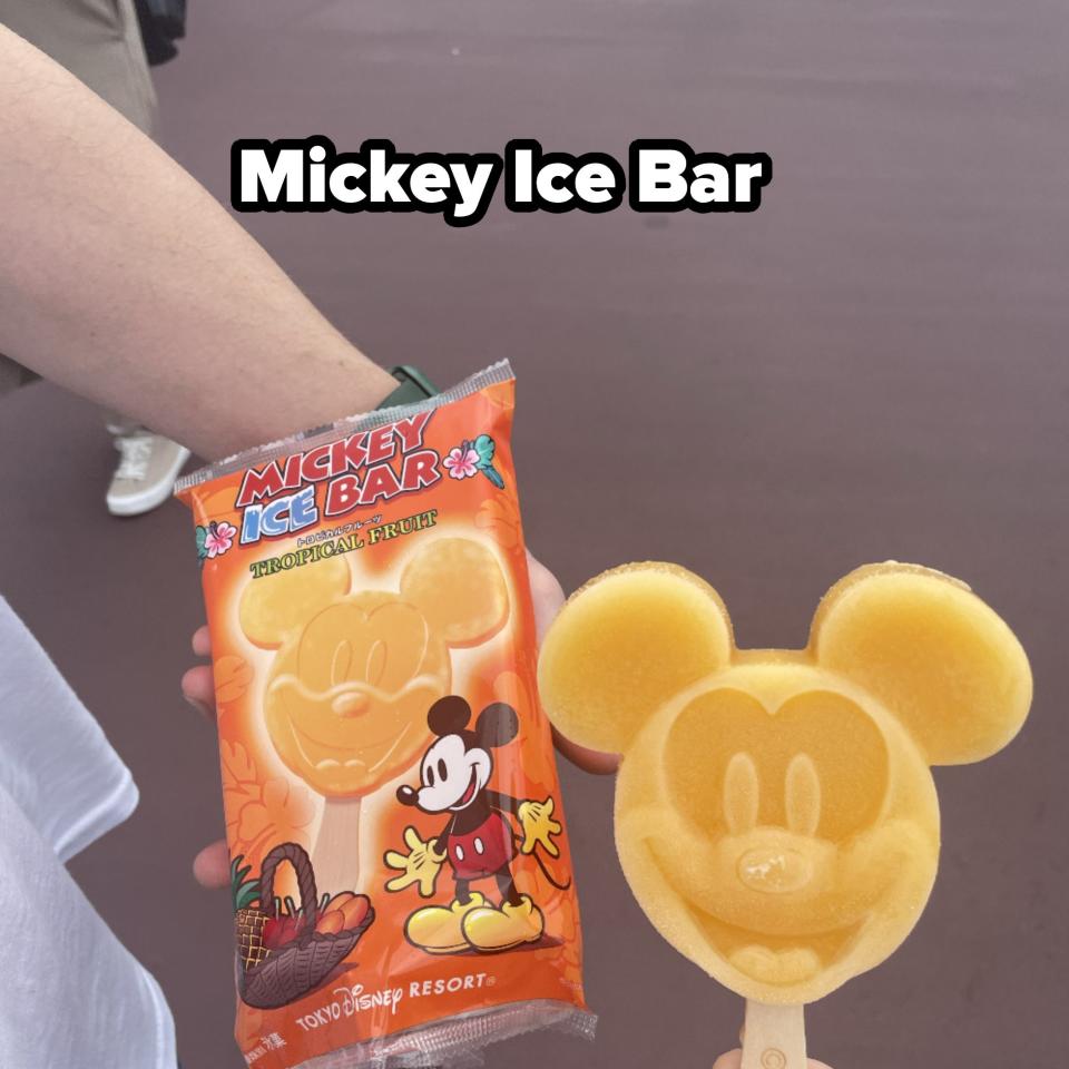 Person holding a Mickey Mouse-shaped ice cream bar and its packaging featuring Mickey Mouse at Tokyo Disney Resort