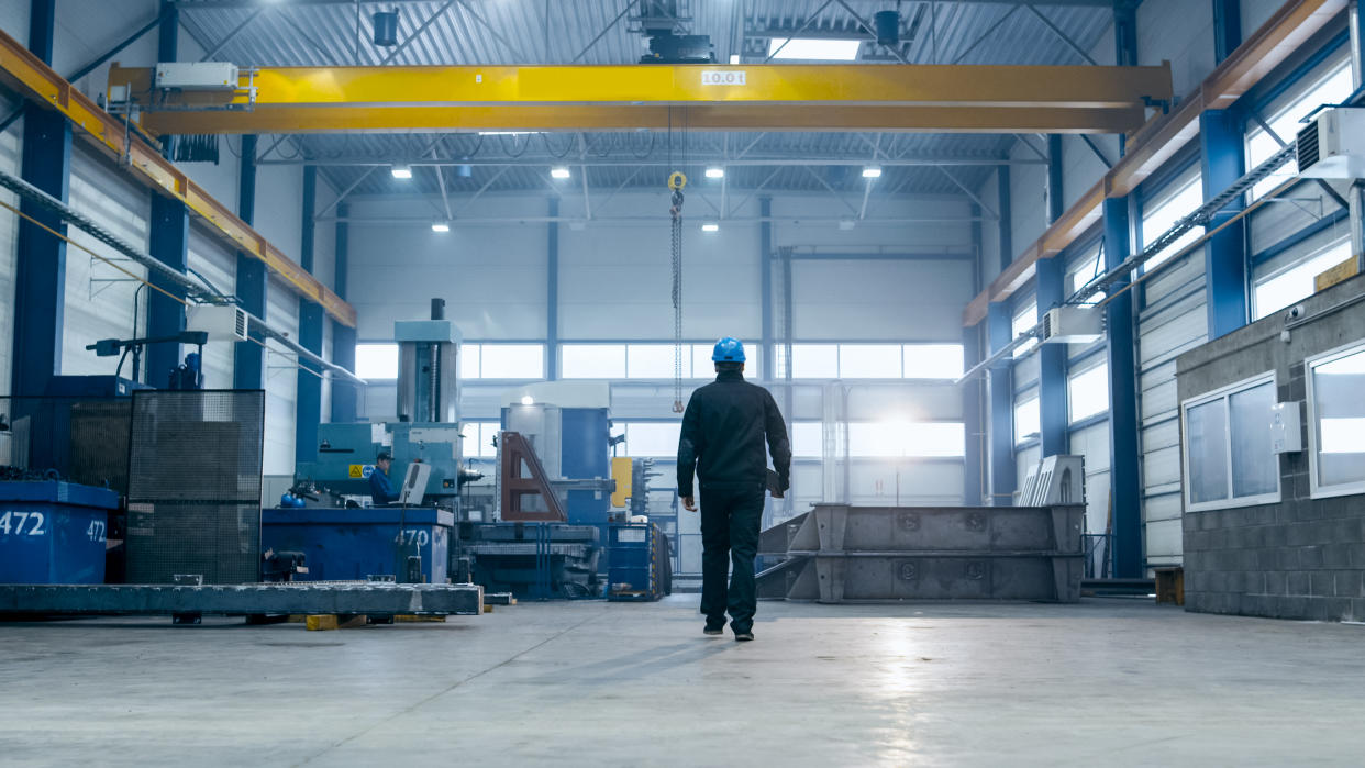 Factory worker in a hard hat is walking through industrial facilities.