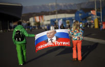 FILE - In this Feb. 23, 2014 file photo Veleriya Obarevich, right, and Yan Shamilov carry a Russian flag with the message "Thank you, Putin!" written across it in Russian through Olympic Park ahead of the 2014 Winter Olympics closing ceremony in Sochi, Russia. The World Anti-Doping Agency banned Russia on Monday Dec. 9, 2019 from the Olympics and other major sporting events for four years, though many athletes will likely be allowed to compete as neutral athletes. (AP Photo/David Goldman, file)