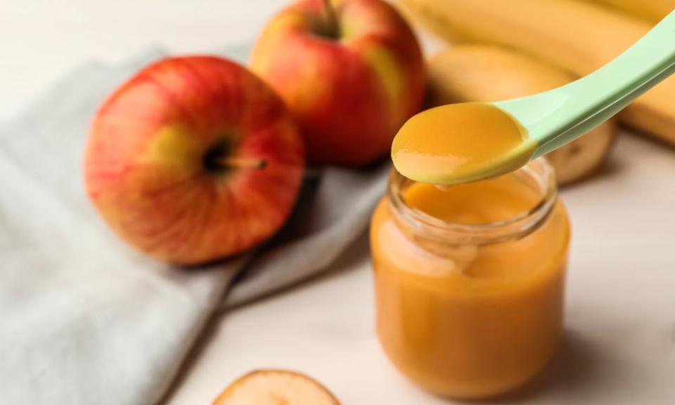 Spoon with baby food over glass jar on white wooden table, closeup