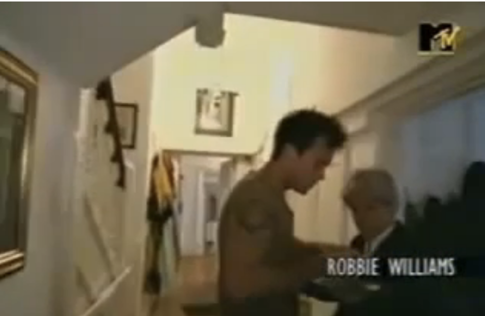 Robbie Williams in a scene from MTV Cribs UK, taking a cigarette from his butler