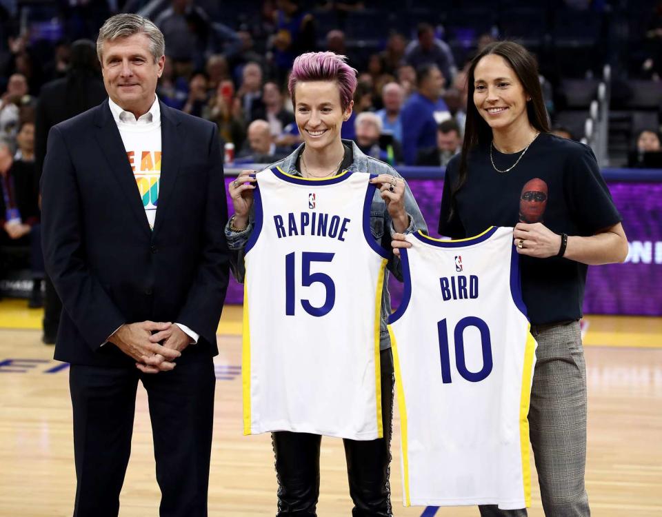 Megan Rapinoe and WNBA star Sue Bird are given Golden State Warriors' jerseys by Warriors President & Chief Operating Officer Rick Welts during a time out of their game against the Phoenix Suns at Chase Center on October 30, 2019 in San Francisco, California. NOTE TO USER: User expressly acknowledges and agrees that, by downloading and or using this photograph, User is consenting to the terms and conditions of the Getty Images License Agreement