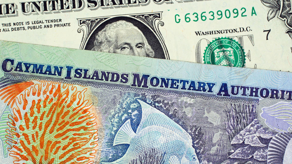 A close up image of a colorful Cayman Islands dollar bill with an American one dollar bill.