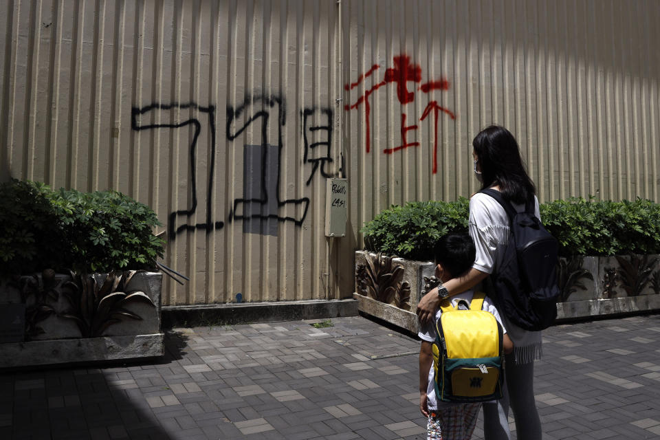 Pamela Lam and her son stand in Hong Kong, Friday, July 3, 2020. Lam's 6-year-old son fell in love with the Hong Kong protest anthem, "Glory to Hong Kong," the first time he heard it and sings it quite often. The Chinese painted on wall reads: "See you on street at July 1." Lam agreed to be photographed only if her face was not shown, fearing possible retribution from authorities. (AP Photo/Kin Cheung)