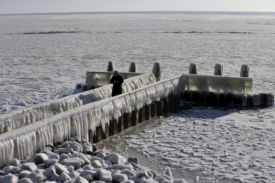 A woman takes pictures of icicles on a jetty at the Afsluitdijk, a dike separating IJsselmeer inland sea, and the Wadden Sea, Netherlands, Thursday, Feb. 11, 2021. The deep freeze gripping parts of Europe served up fun and frustration with heavy snow cutting power to some 37,000 homes in central Slovakia. (AP Photo/Peter Dejong)