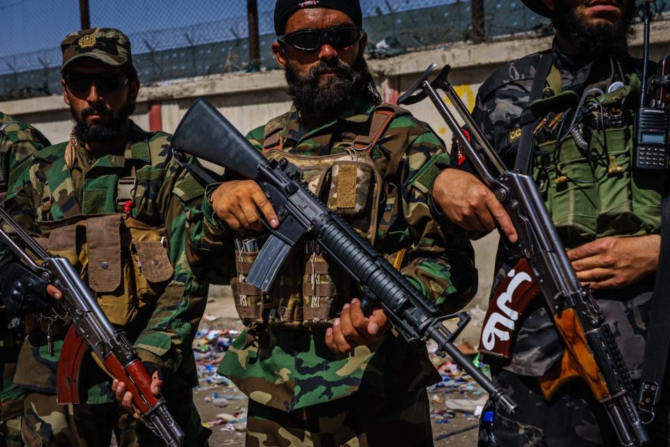 Taliban fighters with rifles stand near a fence