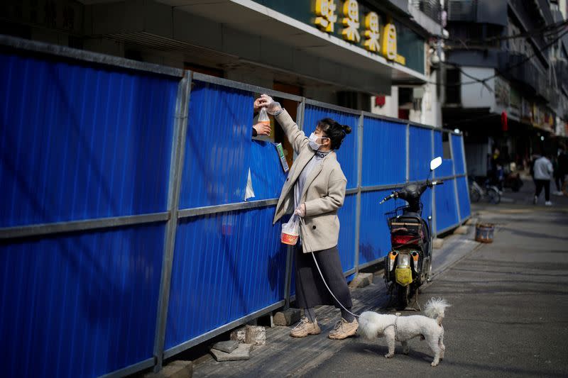 Woman receives food purchased from a store through barricades set up to block buildings from a street in Wuhan
