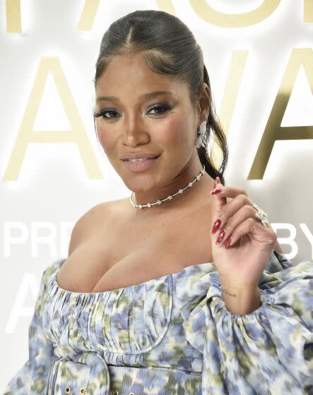 Keke Palmer in a blue patterned dress holding up her left hand