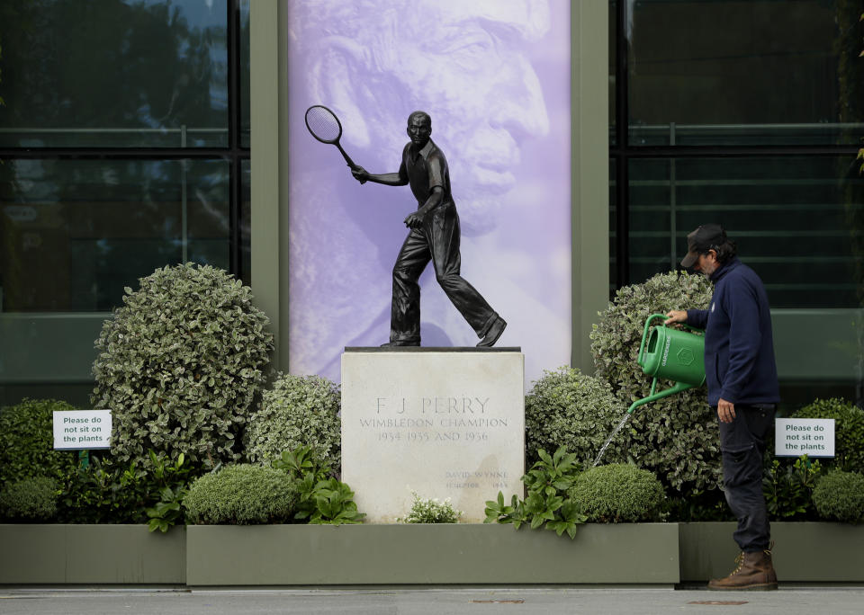 A gardener waters the plants alongside a statue of former Wimbledon Champion Fred Perry at the All England Lawn Tennis Club in Wimbledon in London, Monday, June 29, 2020. The 2020 Wimbledon Tennis Championships, that were due to start today but have been cancelled due to the Coronavirus pandemic. (AP Photo/Kirsty Wigglesworth)