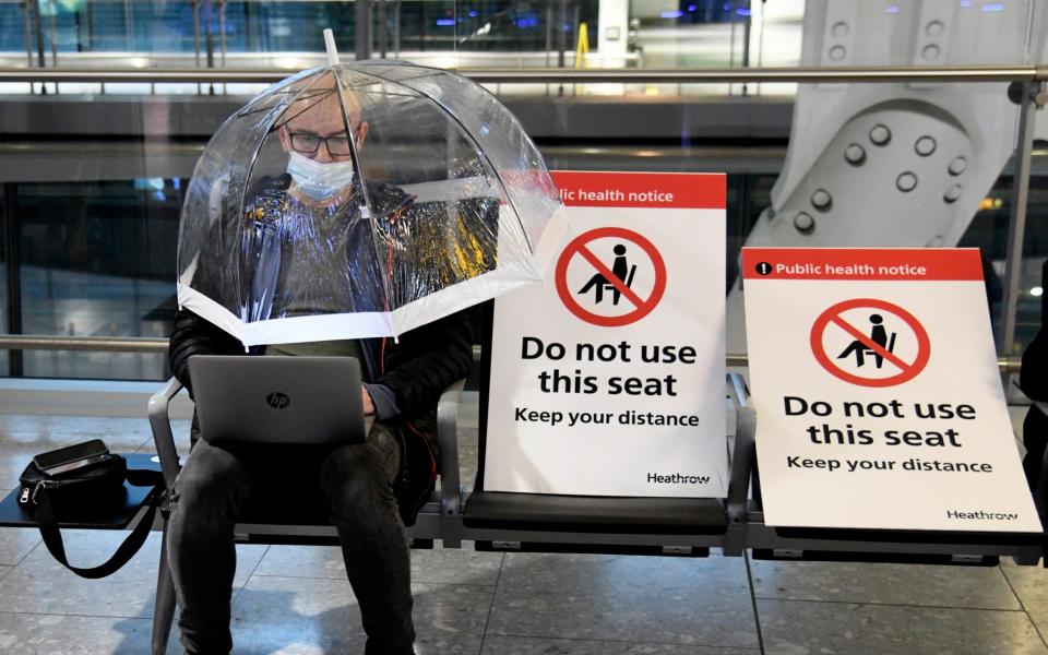 A passenger working on his laptop at the Terminal 5 departure area, Heathrow, shelters unde a transparent umbrella for added protection against coronavirus