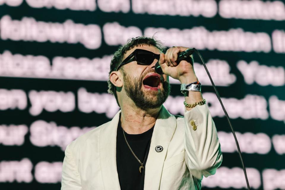 A man sings into a microphone while words appear on a screen behind him.