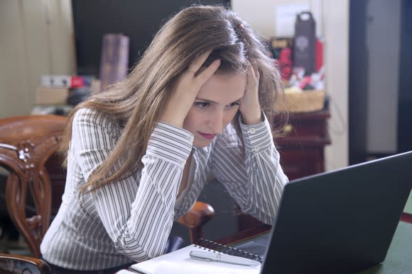 A frustrated investor grasping the top of her head as she looks at stock quotes on her laptop.