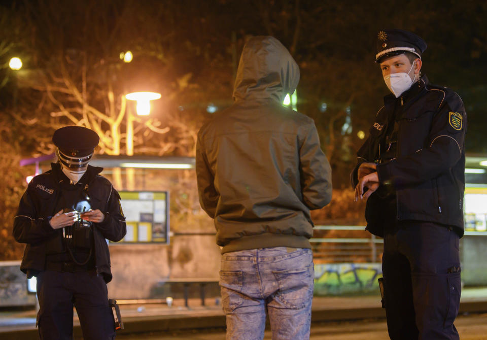 Police officers talk to a man during a curfew check at night in the Gorbitz district in Dresden, Germany, Saturday, Dec. 19, 2020. A hard lockdown has come into force in Germany to contain the coronavirus pandemic. (Robert Michael/dpa via AP)