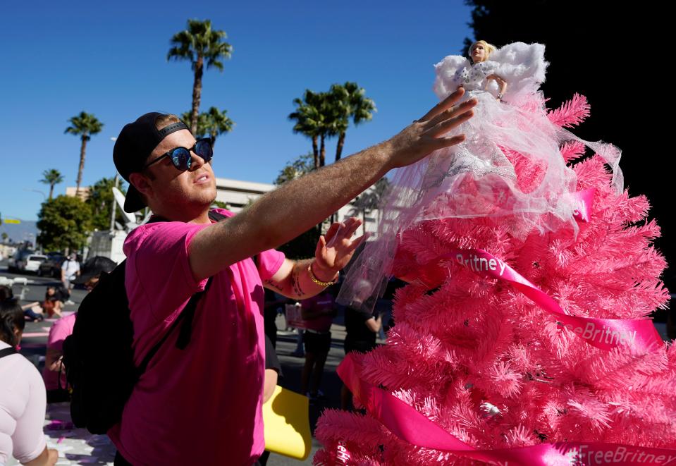 Britney Spears supporter Saige Douglas, of Denver, Col., decorates a "Free Britney" Christmas tree with a Britney Spears doll he created, outside a hearing concerning the pop singer's conservatorship at the Stanley Mosk Courthouse, Friday, Nov. 12, 2021, in Los Angeles. (AP Photo/Chris Pizzello) ORG XMIT: CACP101