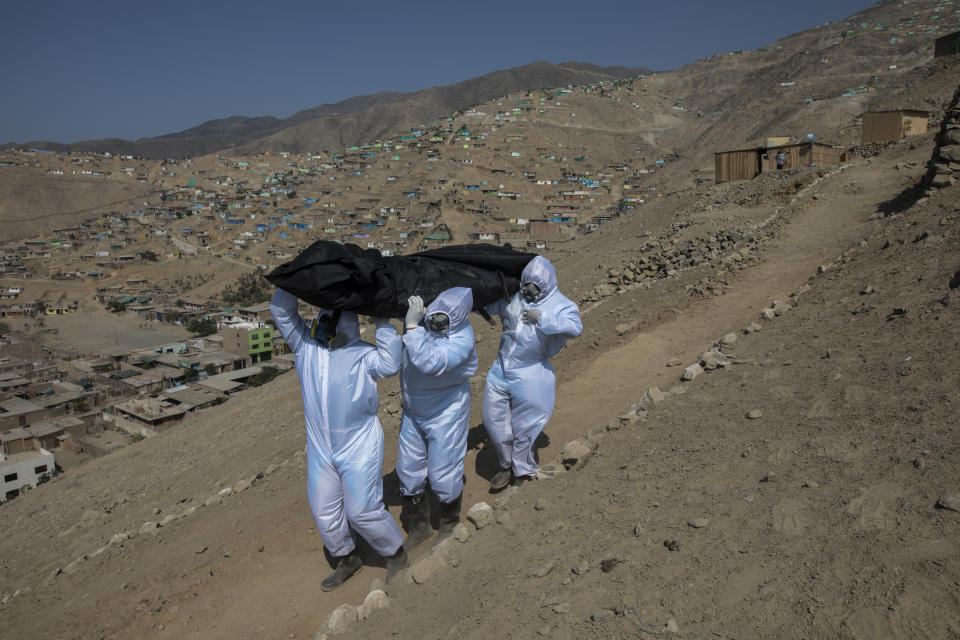 Venezuelan migrants Luis Zerpa leads Luis Brito and Jhoan Faneite to carry the remains of 51-year-old Marcos Espinoza who is suspected fo dying of the new coronavirus, down a steep hill to a waiting hearse in a working-class neighborhood near Pachacamac, the site of an Inca temple, on the outskirts of Lima, Peru, Friday, May 8, 2020. (AP Photo/Rodrigo Abd)