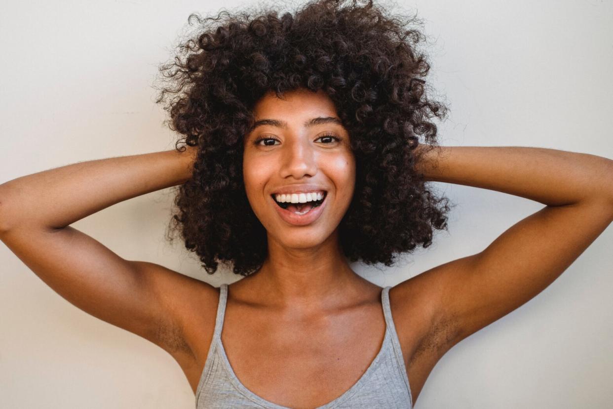 Black woman wearing a grey tank top holding head with both hands on curly hair with grey background