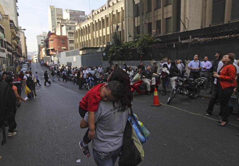 Public employees stand outside their office buildings as they wait for power to be restored, in downtown Caracas, Venezuela, Tuesday, March 25, 2014. A forest fire cut electricity to most of Venezuela's capital and officials were still struggling to restore power to some areas Tuesday, 14 hours after the lights went out. (AP Photo/Fernando Llano)