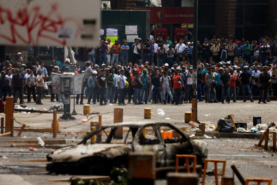 Motorcyclists watch Bolivarian National Guards arrive after the motorcyclists tried to remove street barricades placed anti-government protesters, which broke out in clashes between them and the residents of Los Ruices neighborhood in Caracas, Venezuela, Thursday, March 6, 2014. The car in the foreground was burned during the clashes that officials say killed a National Guard member and a civilian. (AP Photo/Fernando Llano)