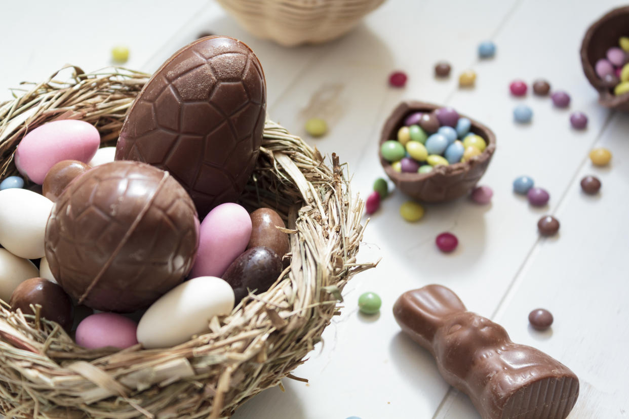 Chocolate eggs and easter almonds on bird nest, chocolate bunny and sweets on white wooden table