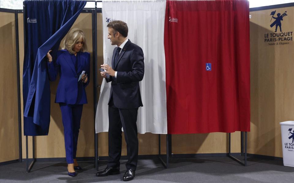 France's President Emmanuel Macron (R), flanked by his wife Brigitte Macron (L), exits a polling booth, adorned with curtains displaying the colors of the flag of France, to vote in the second round of France's legislative election at a polling station in Le Touquet, northern France on July 7, 2024. France votes in legislative elections on July 7, 2024 that will be decisive in determining its political future and could see the far right become the largest party in parliament for the first time. (Photo by MOHAMMED BADRA / POOL / AFP) (Photo by MOHAMMED BADRA/POOL/AFP via Getty Images)