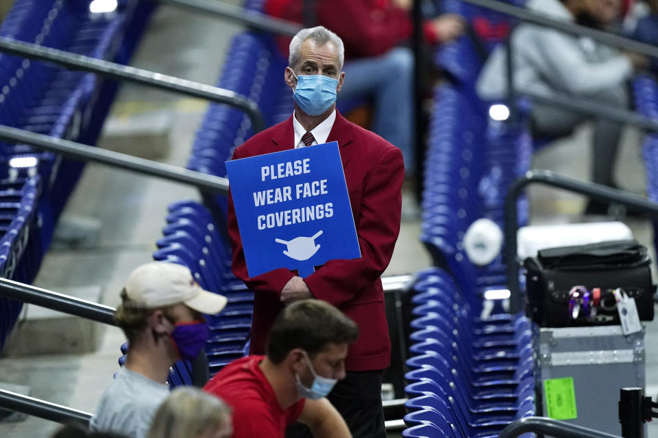 FILE - In this March 21, 2021, file photo, an usher holds a sign reminding fans to wear masks during a college basketball game between Houston and Rutgers in the second round of the NCAA tournament at Lucas Oil Stadium in Indianapolis. President Joe Biden's pleas for states to stick with mask mandates to slow the spread of the coronavirus were being largely ignored Tuesday, March 30, as several Republican governors stayed on track to drop the requirement in their states. (AP Photo/Mark Humphrey, File)