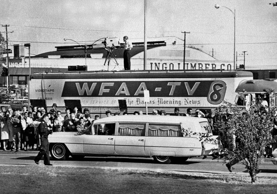FILE - In this Nov. 22, 1963 file photo, people line the street as the hearse bearing the body of slain U.S. President John F. Kennedy drives past a television truck as it leaves Parkland Hospital in Dallas, to be flown to Washington. (AP Photo/File)