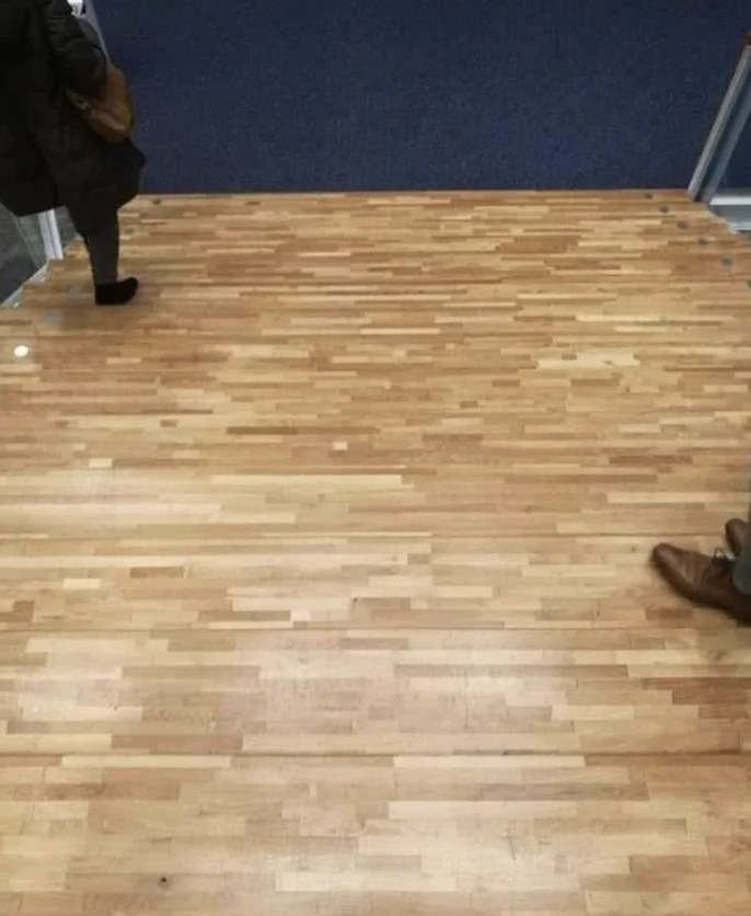 Person's feet at the edge of a flawlessly camouflaged door on the floor, creating an optical illusion