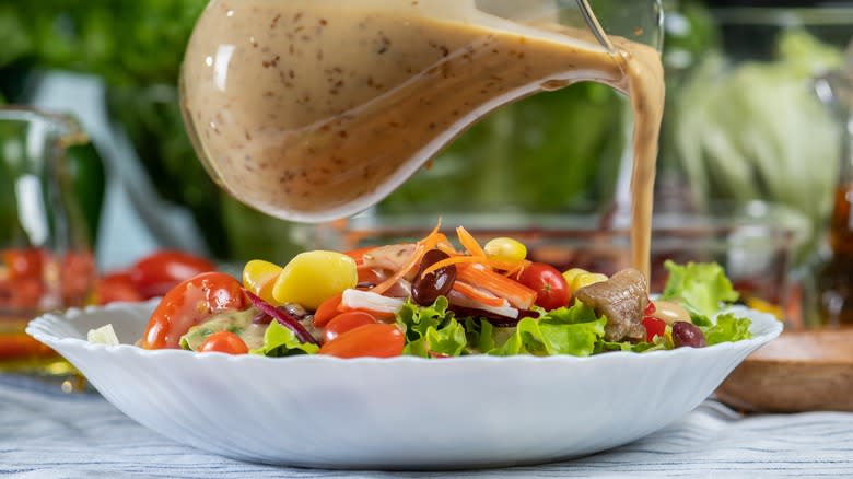 Pouring carafe of creamy dressing over salad