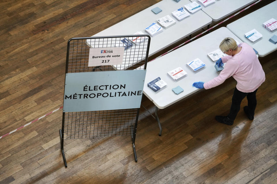 A volunteer cleans the table where the ballots are displayed for local elections in Lyon, central France, Sunday, March 15, 2020. France is holding nationwide elections Sunday to choose all of its mayors and other local leaders despite a crackdown on public gatherings because of the new virus. For most people, the new coronavirus causes only mild or moderate symptoms. For some it can cause more severe illness. (AP Photo/Laurent Cipriani)