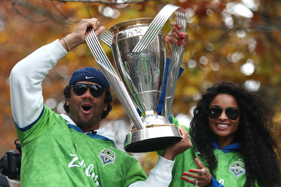 Russell holding up a trophy as Ciara smiles while standing next to him