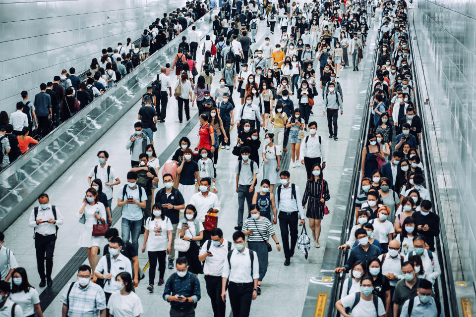 Crowd of busy commuters with protective face mask walking through platforms at subway station during office peak hours in the city