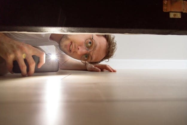 Man looking under a bed with his phone flashlight