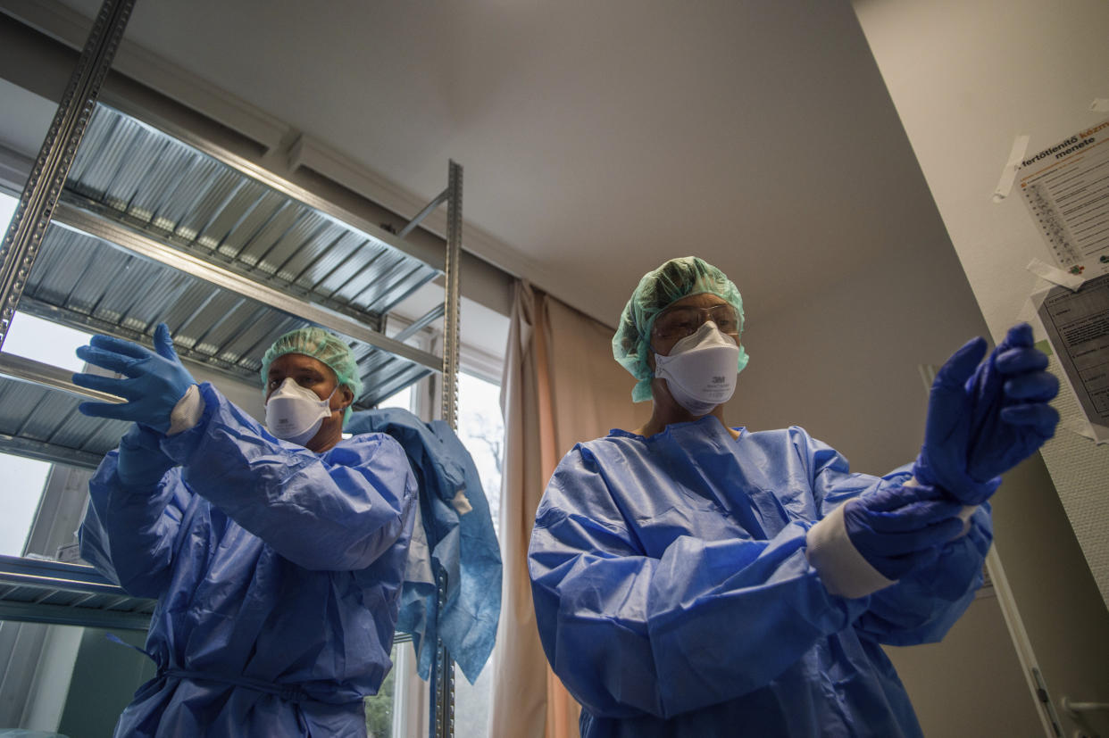 Doctors take on protective suits before they enter the isolation room at the care unit of the new COVID-19infected patients inside the Koranyi National Institute of Pulmonology in Budapest, Hungary, Wednesday, March 25, 2020. (Zoltan Balogh/MTI via AP)