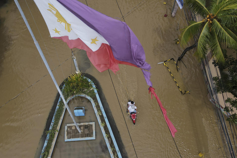 A tattered Philippine flag is seen over a flooded road due to Typhoon Noru in San Miguel town, Bulacan province, Philippines, Monday, Sept. 26, 2022. Typhoon Noru blew out of the northern Philippines on Monday, leaving some people dead, causing floods and power outages and forcing officials to suspend classes and government work in the capital and outlying provinces. (AP Photo/Aaron Favila)