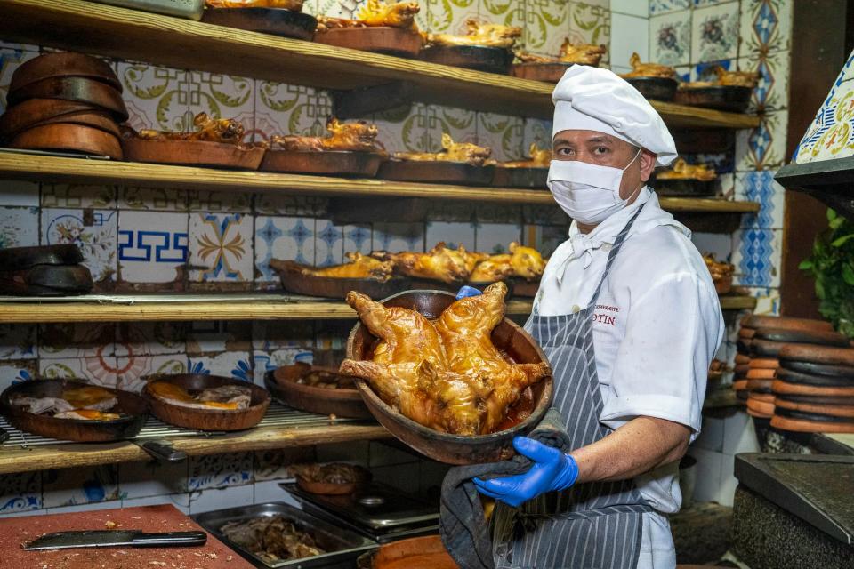 A cook holding a pan with a roast pig.