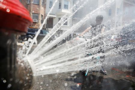 A boy on a bicycle cools off from the extreme heat from an opened fire hydrant in Brooklyn, New York, U.S., July 2, 2018. REUTERS/Shannon Stapleton