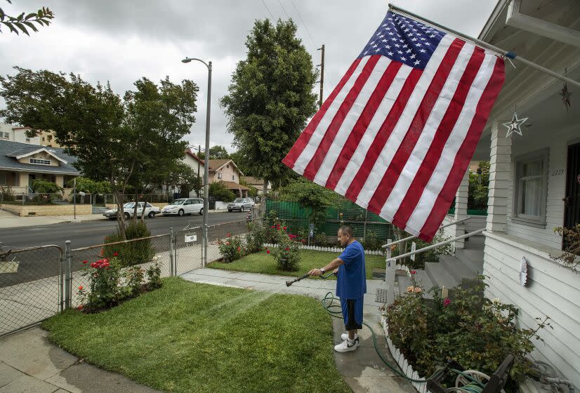 LINCOLN HEIGHTS, CA-MAY 20, 2022: Eddie Vasquez, 61, waters the front lawn of his home on Thomas St. in Lincoln Heights. Vasquez said that he waters the lawn once a week, giving it a good soaking. He has the American flag out in honor of the victims of 9/11 and also because of his nephew, who joined the Marines and is now Staff Sgt. Victor Martinez. It's going to be a summer of brown grass and hard choices for Southern California lawn owners facing the Metropolitan Water District's one day a week watering restrictions starting June 1. (Mel Melcon / Los Angeles Times)