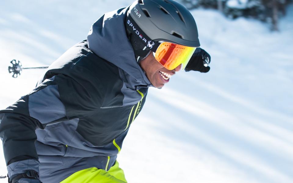 Black man wearing SPYDER goggles while downhill skiing and smiling