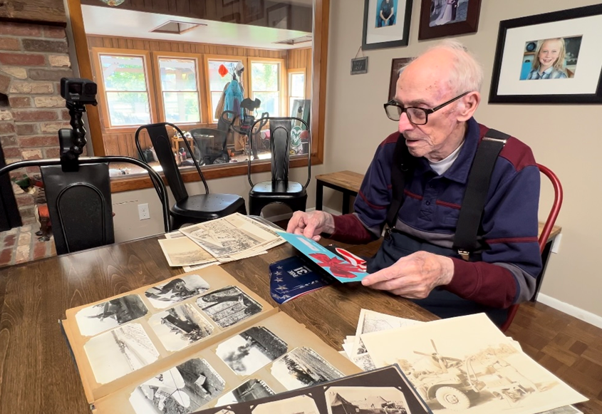 Bill Stremel sits at a table covered with old black-and-white photos while holding a gift card