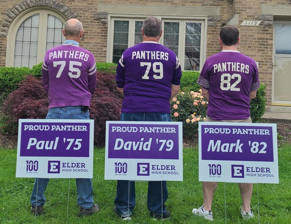 Alumni of Elder High School stand in front of yard signs honoring the school's centennial celebration.