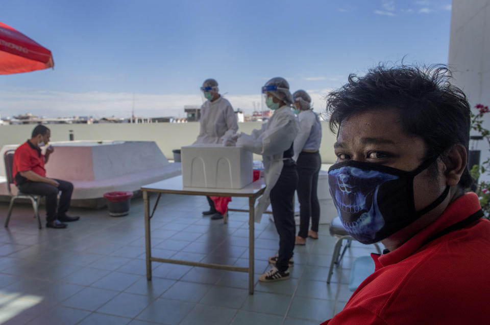 A postal worker in a printed mask waits for his turn to submit a saliva sample for a coronavirus test at a post office rooftop in Bangkok, Thailand, Wednesday, May 27, 2020. Thai health workers started collecting saliva samples of about 200 postal workers in the suburbs of the capital in hopes of curbing the spread of the virus. (AP Photo/Gemunu Amarasinghe)