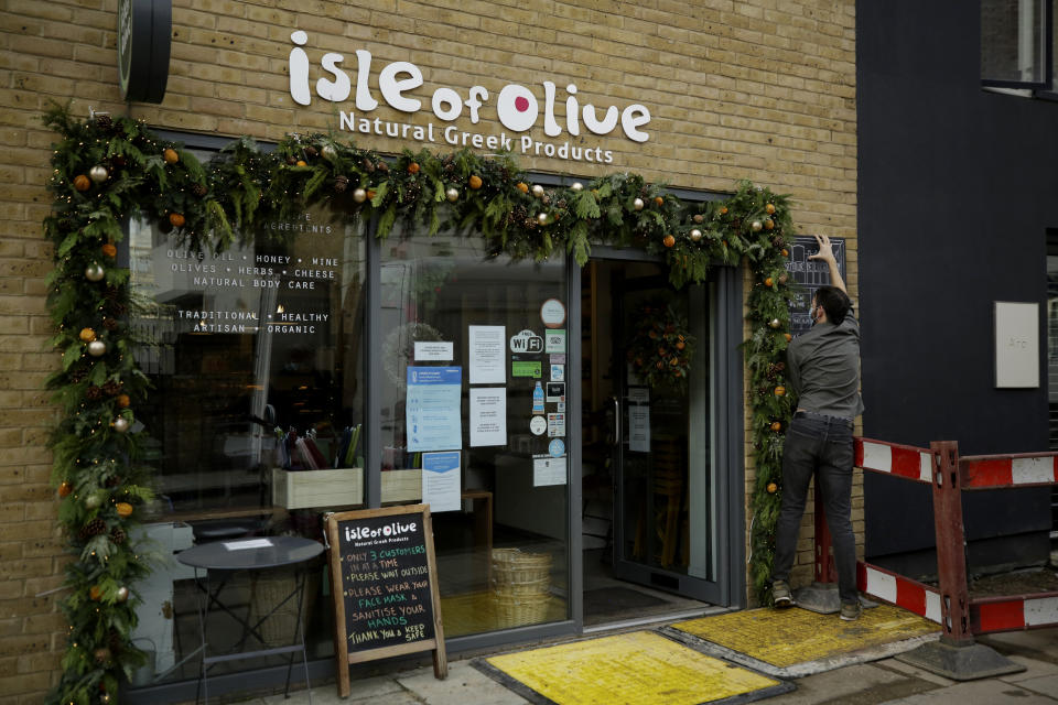 Grigorios Vaitsas puts a sign up outside as he opens up in the morning for trading at his 'Isle of Olive' Natural Greek Products store and delicatessen, which can stay open for takeaway food and drink and online orders during England's second coronavirus lockdown, on Ada Street, off Broadway Market in Hackney, east London, Tuesday, Nov. 17, 2020. Small businesses around the world are fighting for survival amid the economic fallout from the coronavirus pandemic. Whether they make it will affect not just local economies but the fabric of communities.(AP Photo/Matt Dunham)