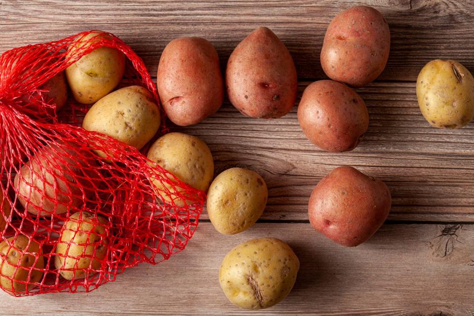 flat lay close up image featuring a red mesh potato sack with pink and yellow raw organic potatoes on wooden background