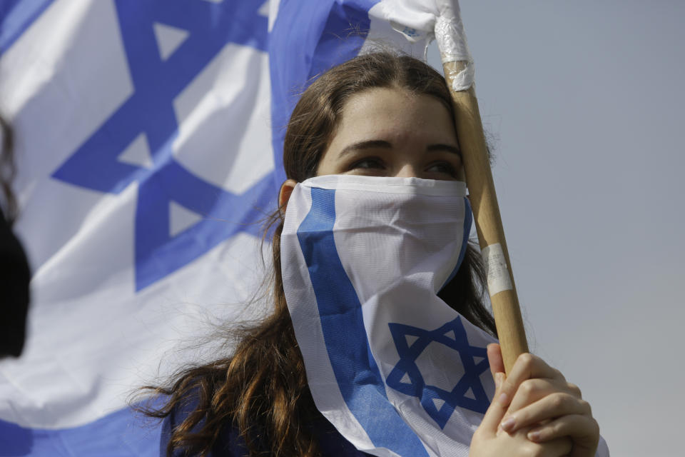 Israeli woman holds national flag during a protest against Prime Minister Benjamin Netanyahu outside the national parliament in Jerusalem, Monday, March 23, 2020. The opposition has accused Netanyahu of using the coronavirus crisis as cover to undermine the country's democratic institutions. With the country in near-shutdown mode, Netanyahu has already managed to postpone his own pending criminal trial and authorize unprecedented electronic surveillance of Israeli citizens. (AP Photo/Sebastian Scheiner)