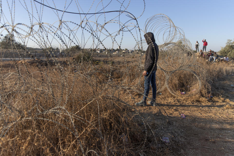 Palestinians gather by a section of Israel's separation barrier, while they wait for the Israeli army to allow them to cross the fence, in the West Bank village of Nilin, west of Ramallah, Sunday, Nov. 7, 2021. Nearly two decades after Israel sparked controversy worldwide by building the barrier during a Palestinian uprising, it has become a seemingly permanent feature of the landscape — even as Israel encourages its citizens to settle on both sides. (AP Photo/Nasser Nasser)