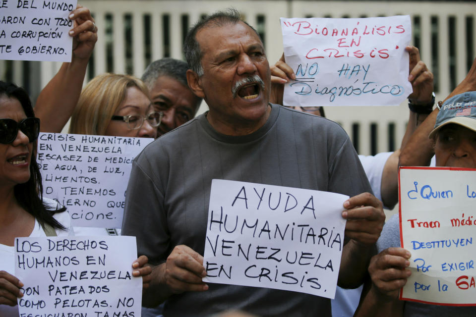 An employee of a children's hospital holds a sign that reads in Spanish "Humanitarian aid, Venezuela in crisis," during a protest by the hospital's workers in Caracas, Venezuela, Thursday, March 14, 2019. The sign at top right reads: "Bioanalysis in crisis. There's no diagnostic," (AP Photo/Fernando Llano)