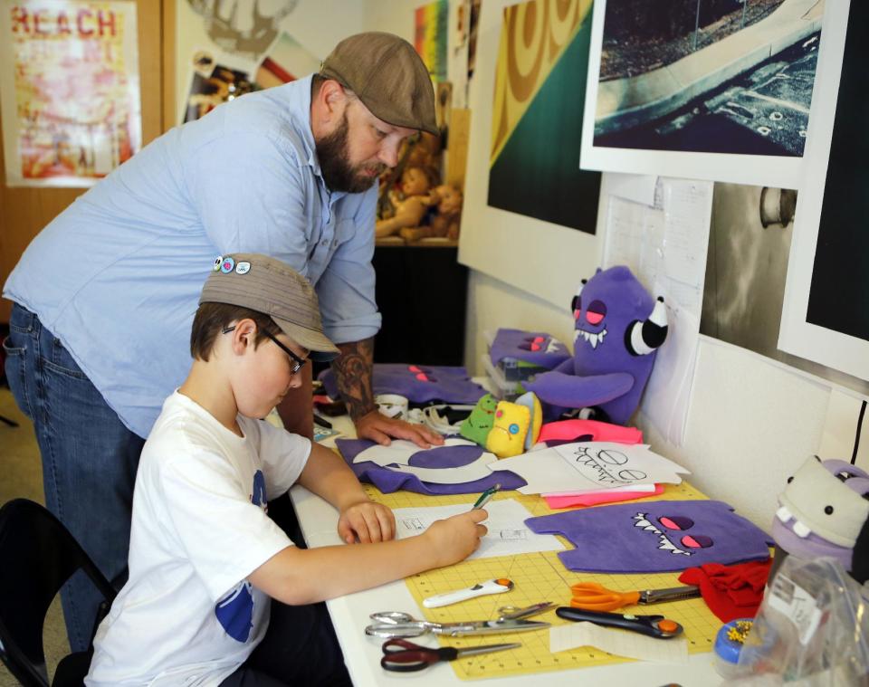 This photo taken on May 23, 2013 shows Ray Tollison looking over the shoulder of his son Sam as he works on a drawing of a monster doll at their home in Fort Collins, Colo. The Tollisons launched Monster to Love, a company that makes plush monster toys. (AP Photo/Ed Andrieski)