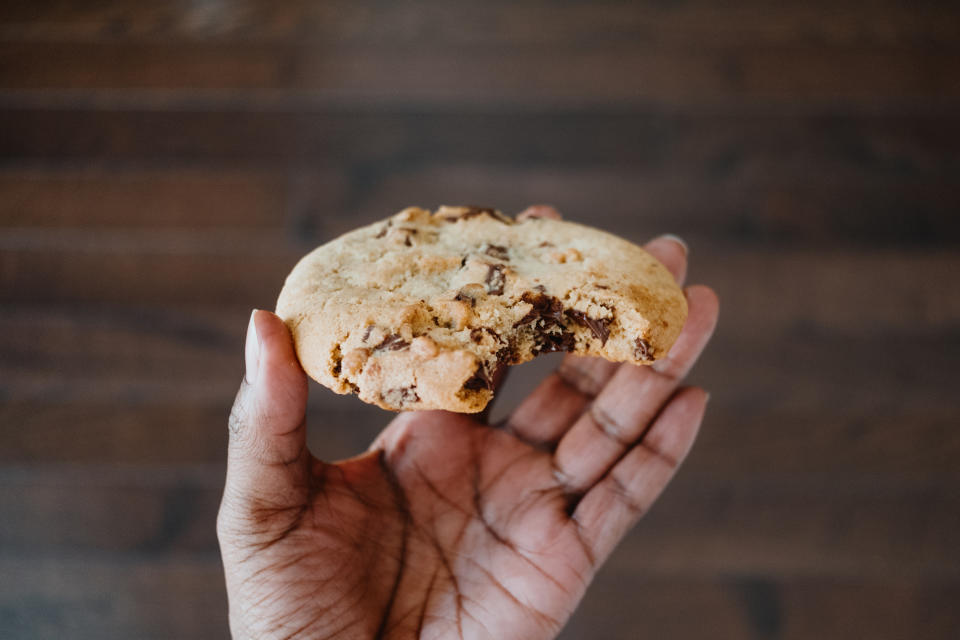 Close-up of unrecognizable black woman holding a giant chocolate chip cookie after taking a bite