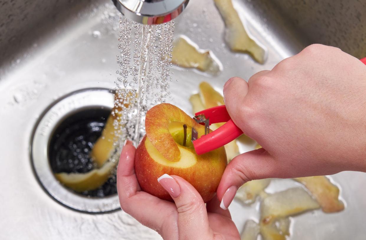 Cropped view of female hands peeling apple over Food waste disposer machine in modern kitchen